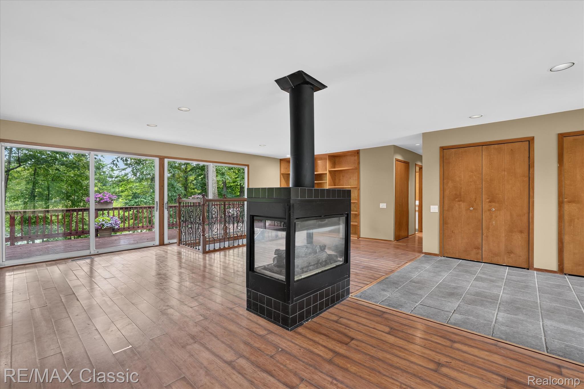 12189 Gage Road Holly, MI 48442 - Photo 6 of 69 Centrally located multi-sided fireplace with black tile surround, wood-finish flooring, recessed lighting, and expansive sliding glass doors opening to an outdoor deck with decorative metal railing