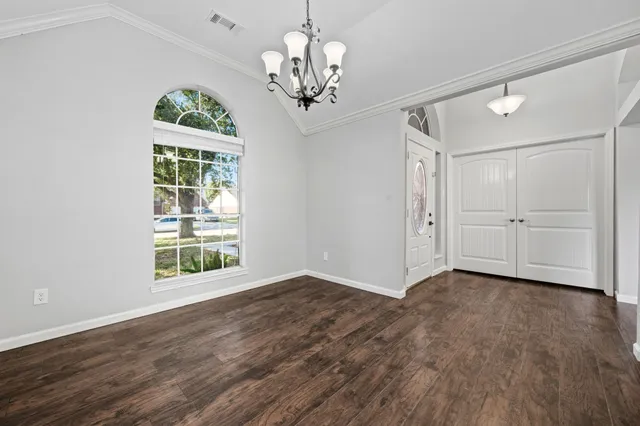 an empty room with wooden floor chandelier and windows