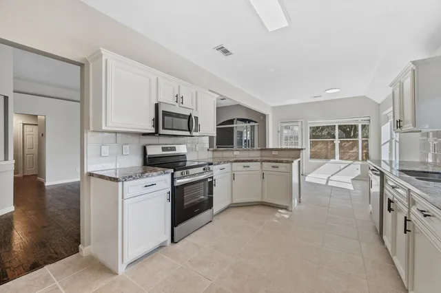 a kitchen with stainless steel appliances granite countertop a stove top oven a sink dishwasher a refrigerator and white cabinets with wooden floor