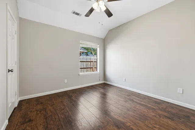 an empty room with wooden floor chandelier fan and windows
