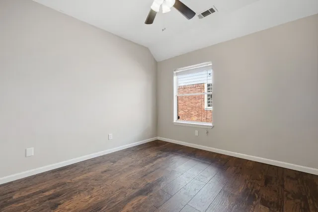 an empty room with wooden floor ceiling fan and window