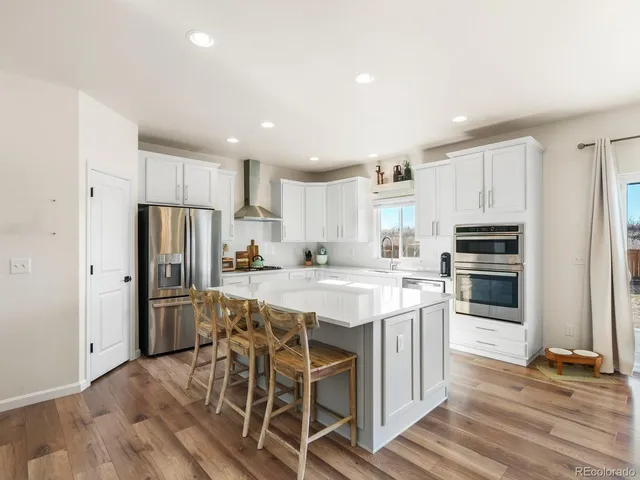 a kitchen with stainless steel appliances a refrigerator a stove a sink dishwasher and white cabinets with wooden floor