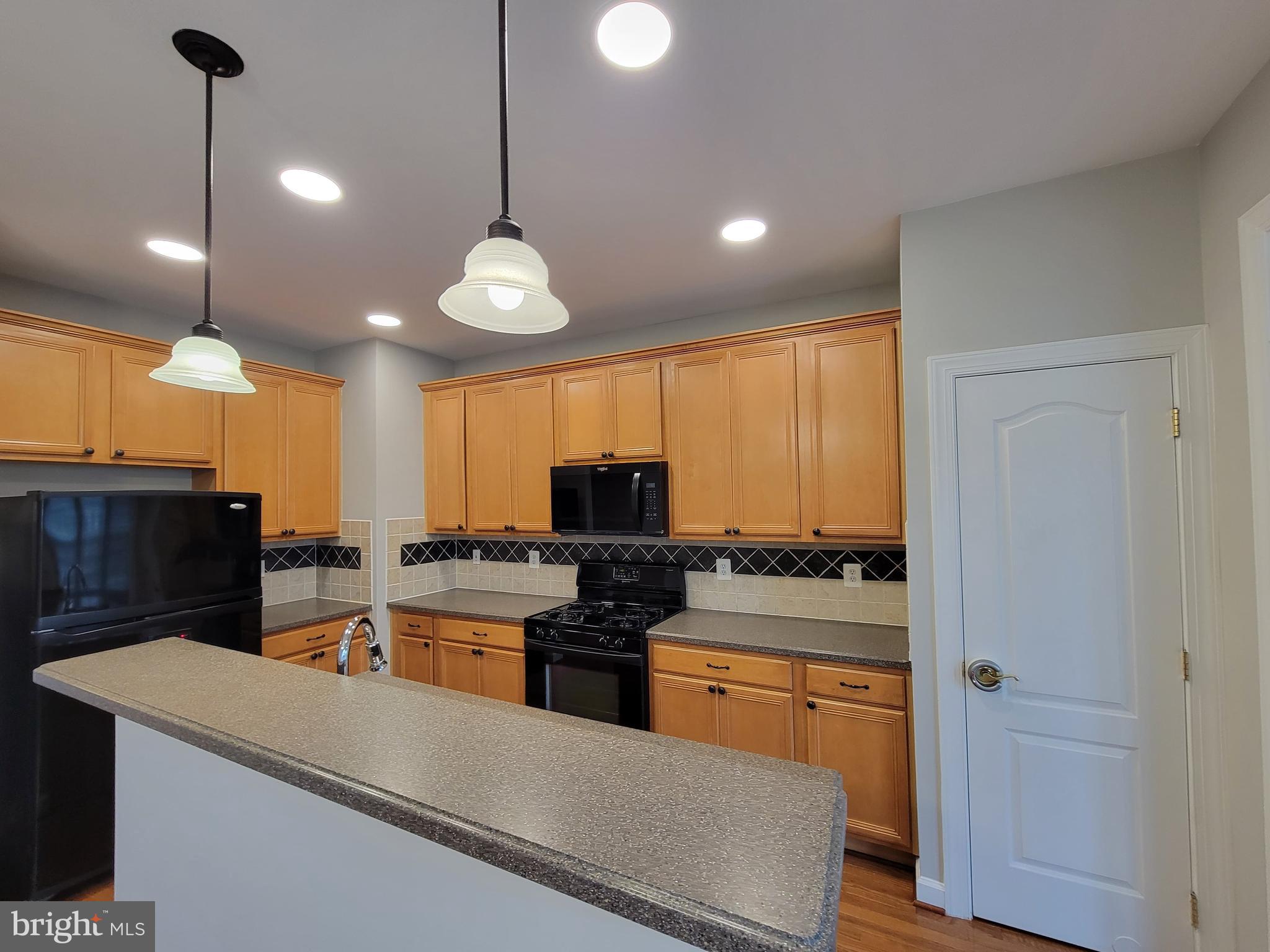11837 Whitworth Cannon Lane Bristow, VA 20136 - Photo 20 of 63 a kitchen with stainless steel appliances kitchen island granite countertop a stove a refrigerator a sink a dining table and chairs with wooden floor