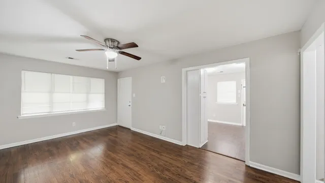 an empty room with wooden floor fan and windows