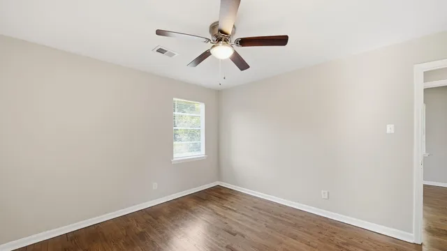 an empty room with wooden floor ceiling fan and windows