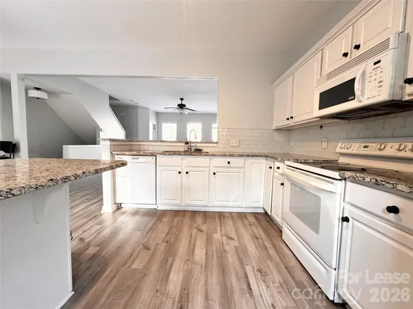 a large white kitchen with stainless steel appliances granite countertop a stove a sink dishwasher and white cabinets with wooden floor