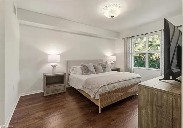 a bedroom with a bed table and a flat tv screen on dresser