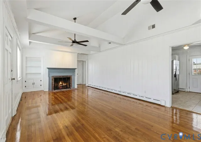 an empty room with wooden floor a ceiling fan a fireplace and windows