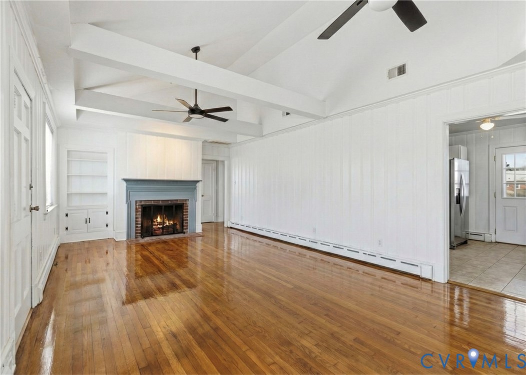 5116 Alberene Road Richmond, VA 23224 - Photo 2 of 20 an empty room with wooden floor a ceiling fan a fireplace and windows