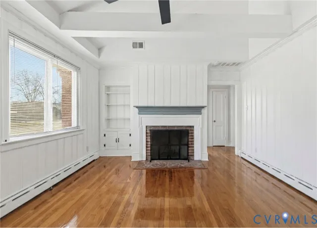 a view of an empty room with wooden floor fireplace and a window