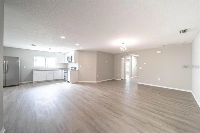 a view of an empty room and a kitchen with wooden floor