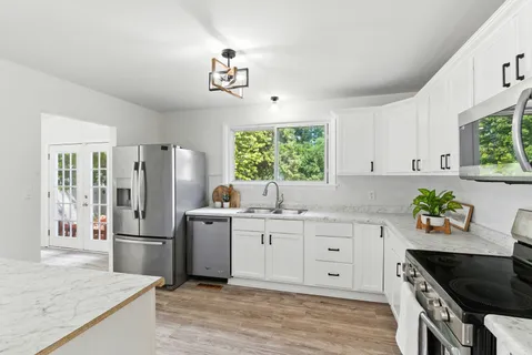 a kitchen with stainless steel appliances granite countertop a refrigerator a sink dishwasher and white cabinets with wooden floor