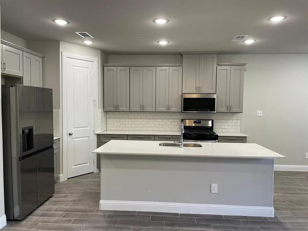 1752 Redding Street Allen, TX 75002 - Photo 6 of 24 Kitchen with backsplash, sink, appliances with stainless steel finishes, and a center island with sink