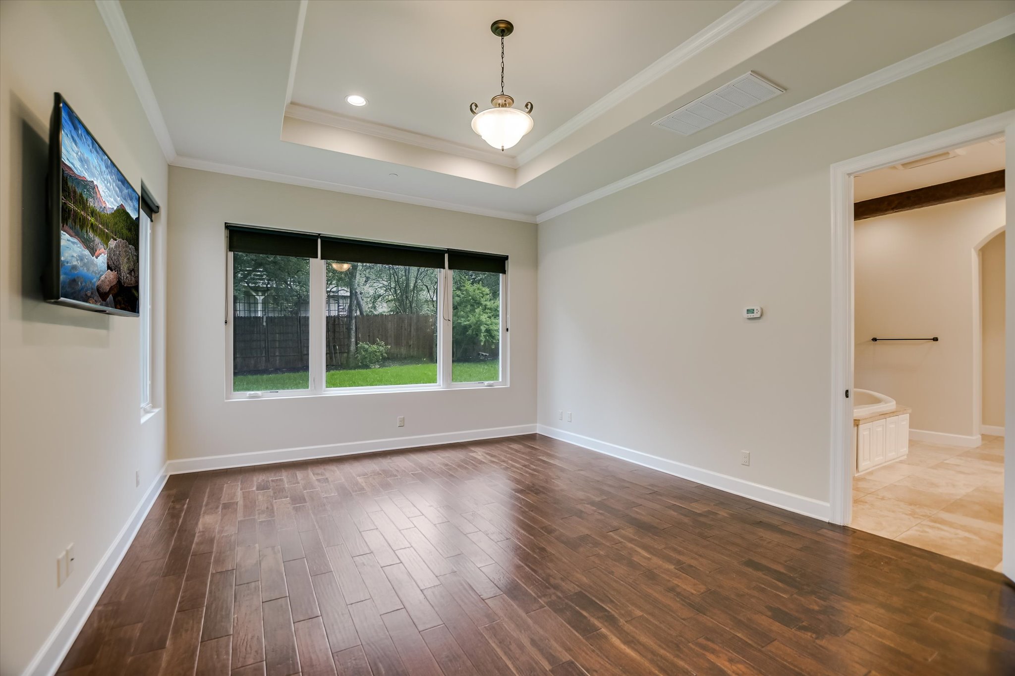 11 Inwood Circle Austin, TX 78746 - Photo 18 of 38 Rich hardwood floors complement tray ceilings in this versatile primary suite, offering a view of the green landscape.