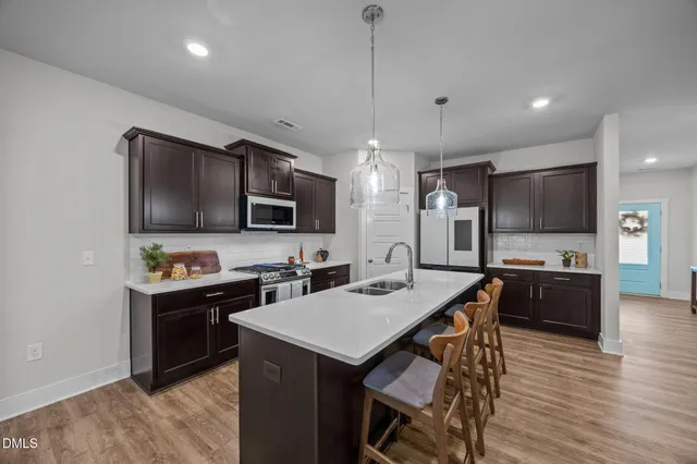 a kitchen with stainless steel appliances kitchen island granite countertop a dining table chairs refrigerator and microwave
