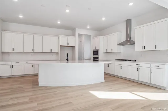 a large white kitchen with wooden floor and stainless steel appliances