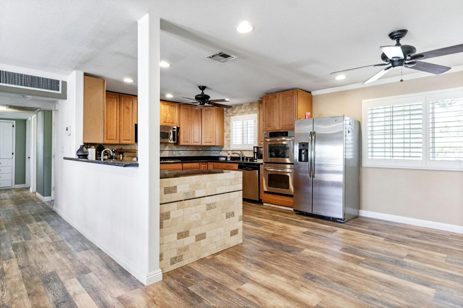 16972 Monreal Road Madera, CA 93636 - Photo 8 of 34 a kitchen with granite countertop a refrigerator oven a sink dishwasher and white cabinets with wooden floor