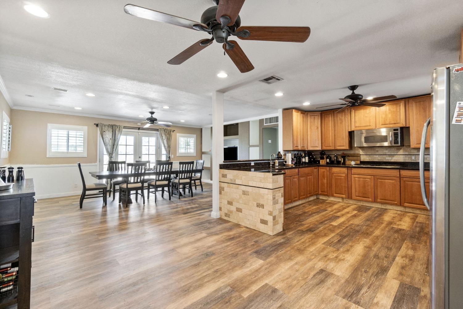16972 Monreal Road Madera, CA 93636 - Photo 9 of 34 a kitchen with stainless steel appliances kitchen island granite countertop a refrigerator a stove a dining table and chairs with wooden floor