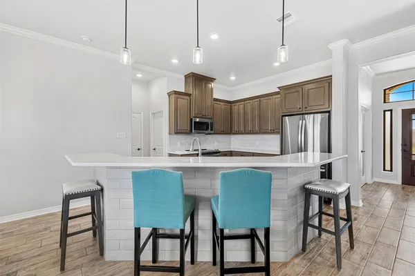 a kitchen with kitchen island granite countertop a table chairs refrigerator and microwave