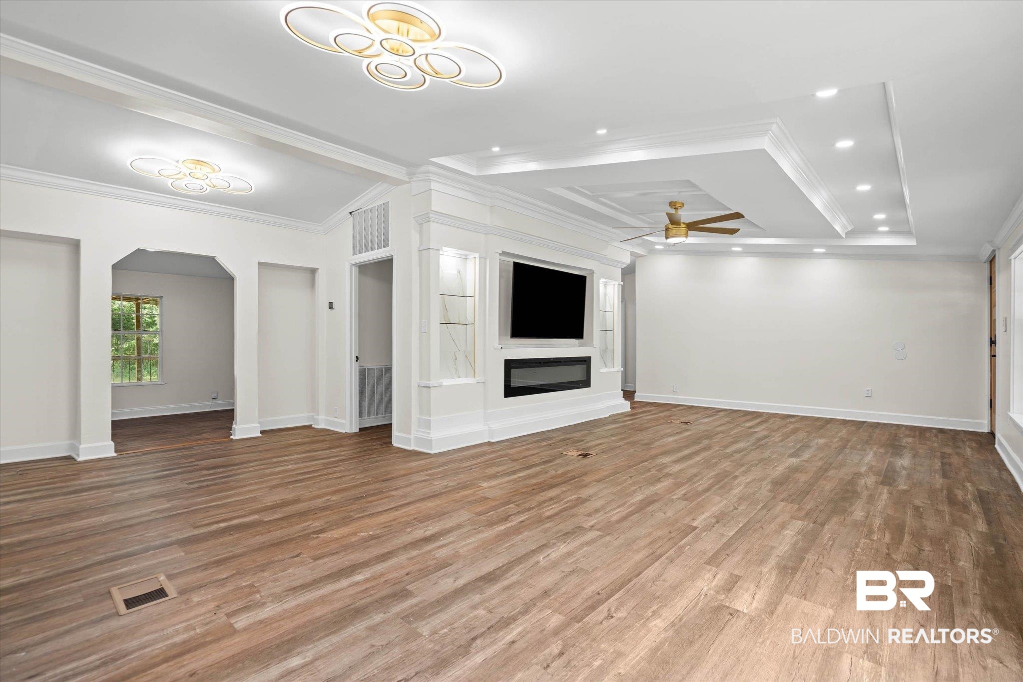 9230 McLeod Road Mobile, AL 36695 - Photo 4 of 20 Spacious living area featuring wood-finish flooring, a built-in media console with an electric fireplace, tray ceilings with recessed lighting, and modern ceiling light fixtures