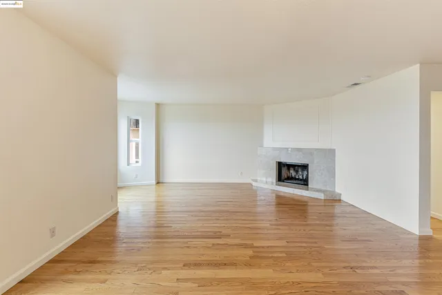 a view of an empty room with wooden floor and a fireplace