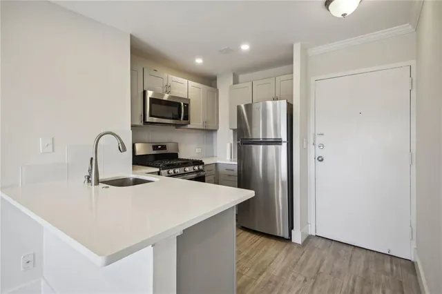 a kitchen with stainless steel appliances granite countertop a refrigerator a sink a stove and white cabinets with wooden floor