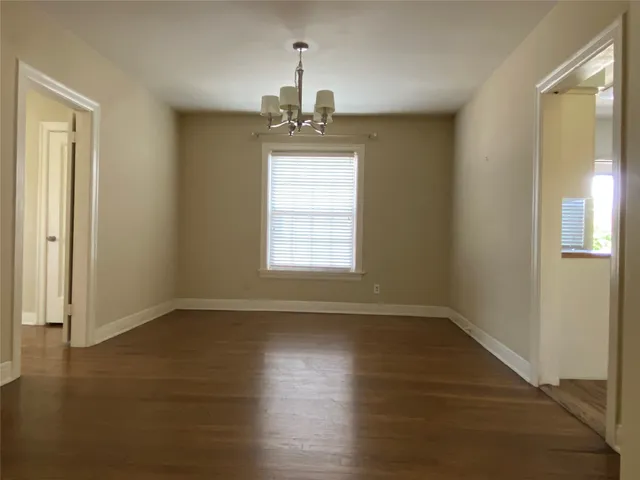 an empty room with wooden floor chandelier and windows