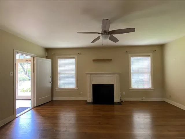 a view of an empty room with wooden floor fireplace and a window