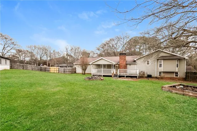 a view of a white house in front of a big yard with plants and large trees