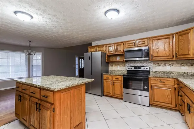 a kitchen with stainless steel appliances granite countertop a stove top oven a sink dishwasher and a refrigerator with wooden cabinets