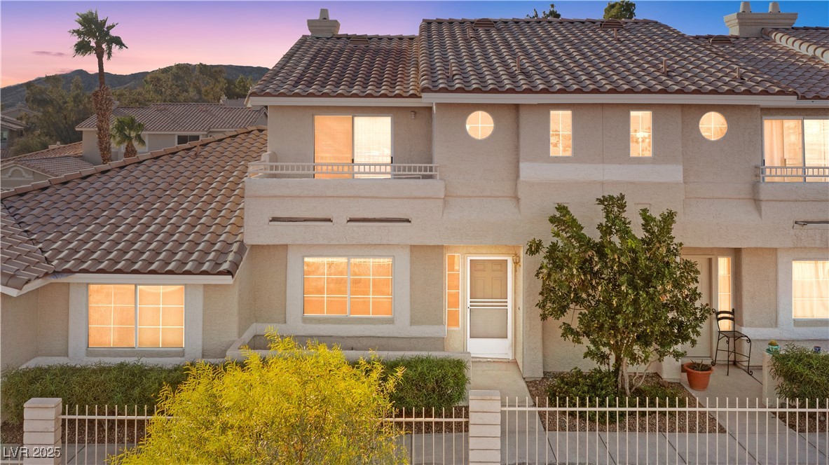 Mediterranean / spanish house featuring a fenced front yard, a balcony, a chimney, stucco siding, and a tiled roof