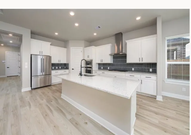 a kitchen with stainless steel appliances kitchen island granite countertop a stove a sink and white cabinets with wooden floor