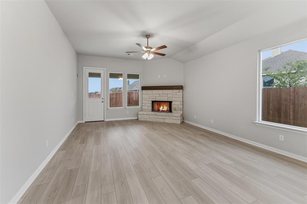 1237 Frio Drive Springtown, TX 76082 - Photo 8 of 25 Living area featuring wood-finish flooring, a stone fireplace with a wood mantel, multiple windows, a ceiling fan, and a door to the exterior