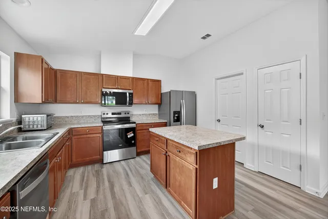 a kitchen with stainless steel appliances granite countertop a stove top oven a sink dishwasher and a refrigerator with wooden cabinets