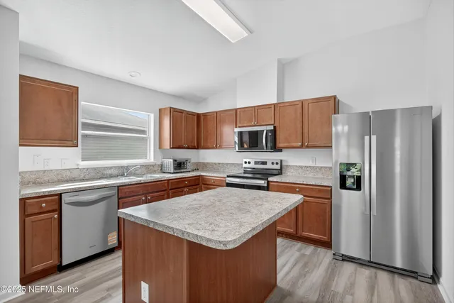 a kitchen with stainless steel appliances granite countertop a stove top oven a refrigerator a sink and dishwasher with wooden floor