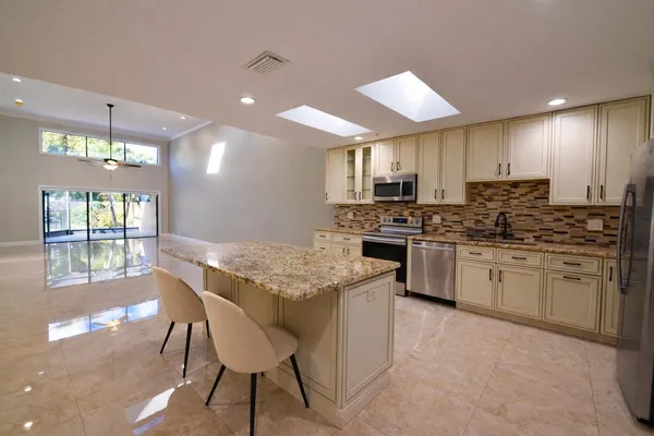 a kitchen with stainless steel appliances kitchen island granite countertop a stove a sink a microwave a dining table and chairs with wooden floor