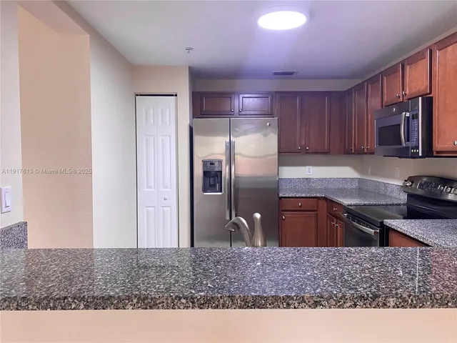 a kitchen with stainless steel appliances granite countertop a refrigerator a stove and a sink with wooden cabinets