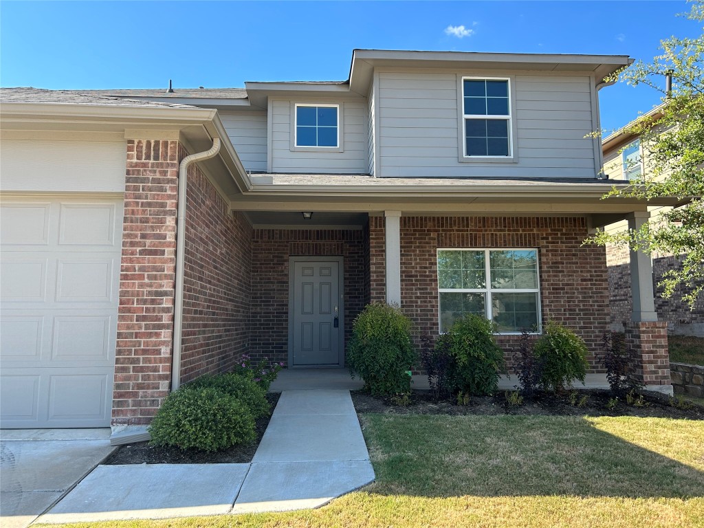 2212 Baugh Road Austin, TX 78754 - Photo 3 of 36 View of exterior entry featuring brick siding, a yard, a garage, and a porch