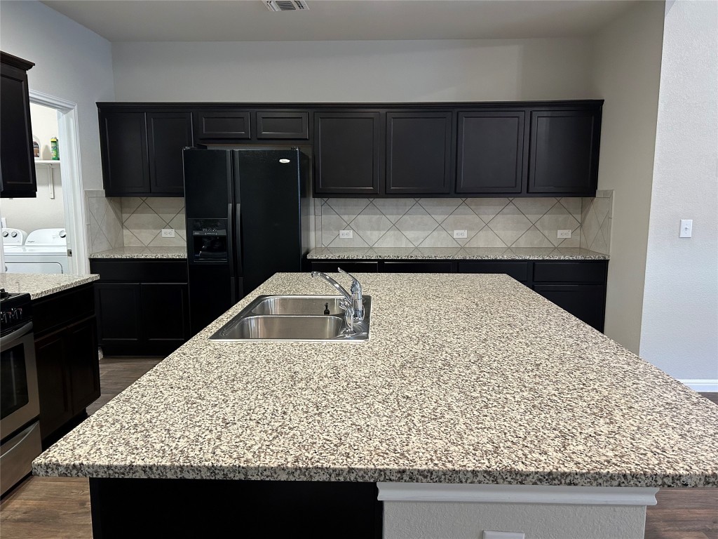 2212 Baugh Road Austin, TX 78754 - Photo 5 of 36 Kitchen with light stone countertops, dark cabinetry, and a kitchen island with sink