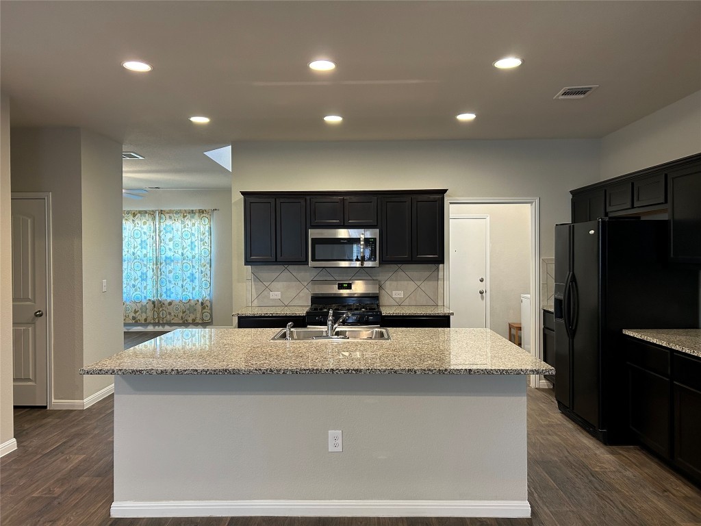 2212 Baugh Road Austin, TX 78754 - Photo 6 of 36 Kitchen featuring appliances with stainless steel finishes, a center island with sink, recessed lighting, light stone countertops, and backsplash