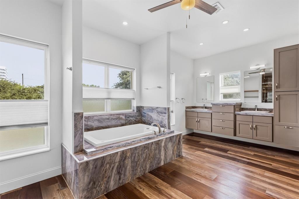 4436 Thunder Road Dallas, TX 75244 - Photo 15 of 33 Spa-like bathroom with wood-finish flooring, a built-in tub with stone surround, dual vanities with integrated sinks, and abundant natural light from multiple windows