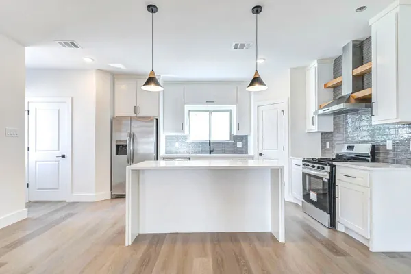 a kitchen with stainless steel appliances granite countertop a stove a sink dishwasher a refrigerator and white cabinets with wooden floor