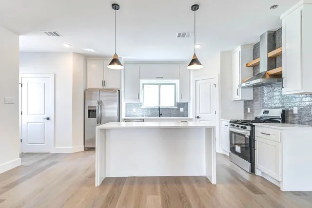 a kitchen with stainless steel appliances granite countertop a stove a sink dishwasher a refrigerator and white cabinets with wooden floor