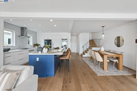 a kitchen with stainless steel appliances granite countertop a refrigerator a stove top oven a dining table and chairs with wooden floor