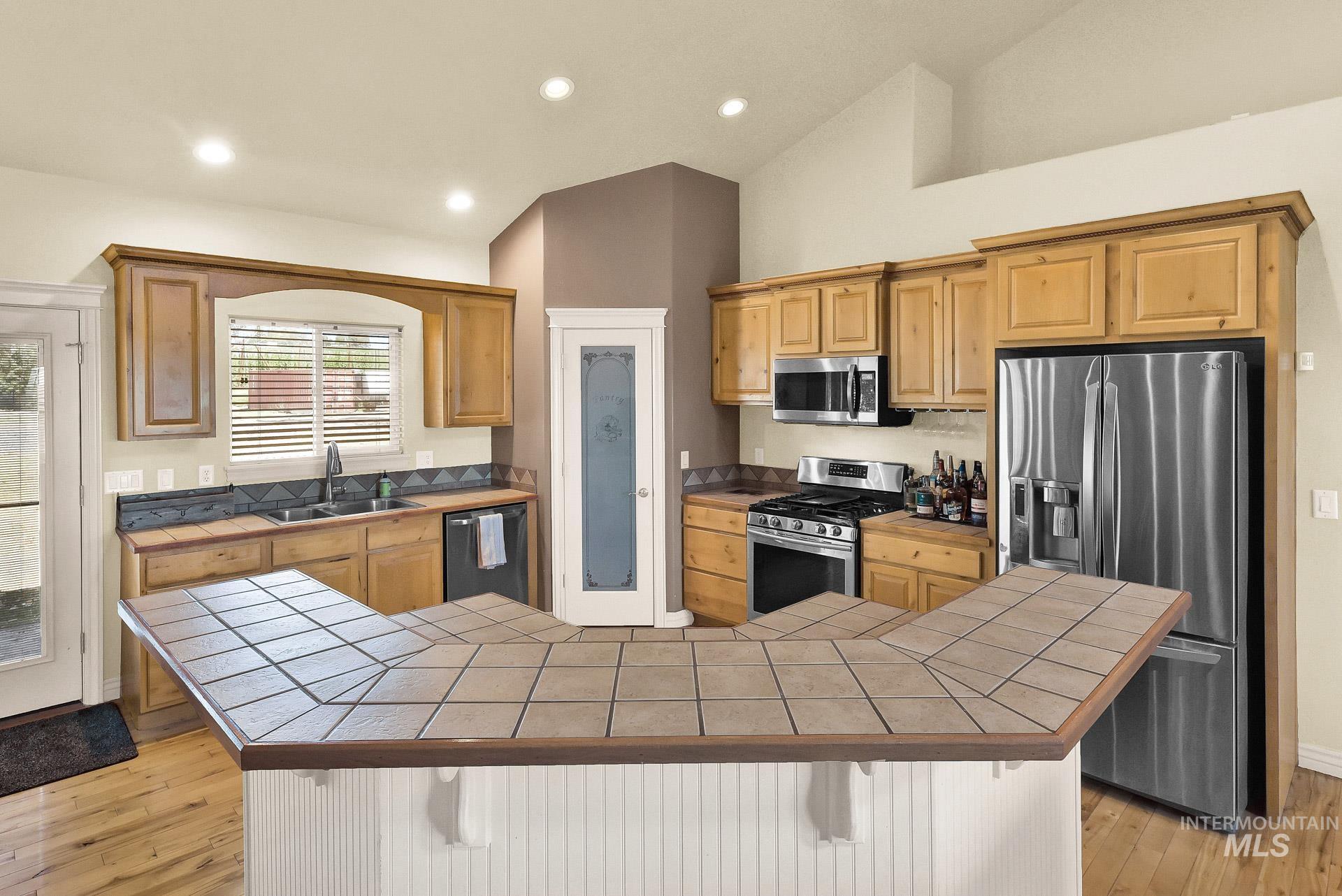 27114 Lower Pleasant Ridge Road Wilder, ID 83676 - Photo 35 of 50 Kitchen featuring tile countertops, a kitchen bar, vaulted ceiling, stainless steel appliances, and light wood-style flooring