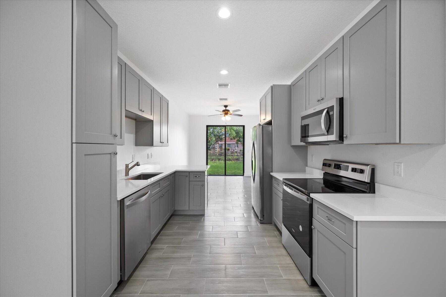 1491 West 30th Street Riviera Beach, FL 33404 - Photo 4 of 15 a large kitchen with stainless steel appliances granite countertop a sink and dishwasher a stove top oven with wooden floor