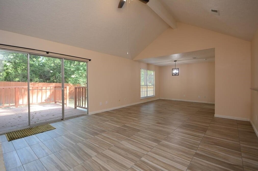 15 South Tallowberry Drive Spring, TX 77381 - Photo 7 of 26 Spacious living area with vaulted ceilings, tile flooring, large sliding glass doors to a wooden deck, and an open layout ideal for entertaining.