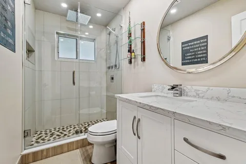 a bathroom with a granite countertop sink a mirror a toilet and shower
