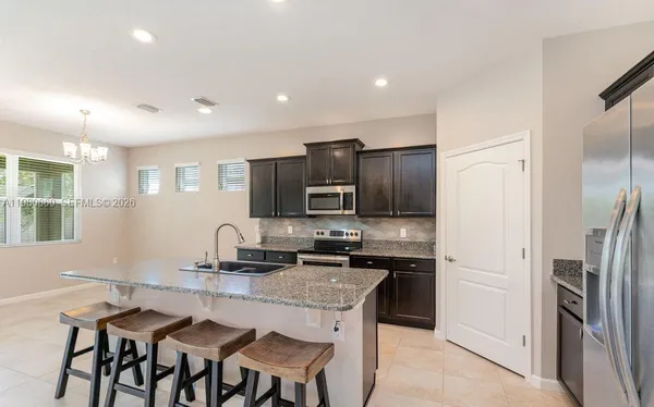 a kitchen with stainless steel appliances granite countertop a refrigerator a stove a sink a dining table and chairs
