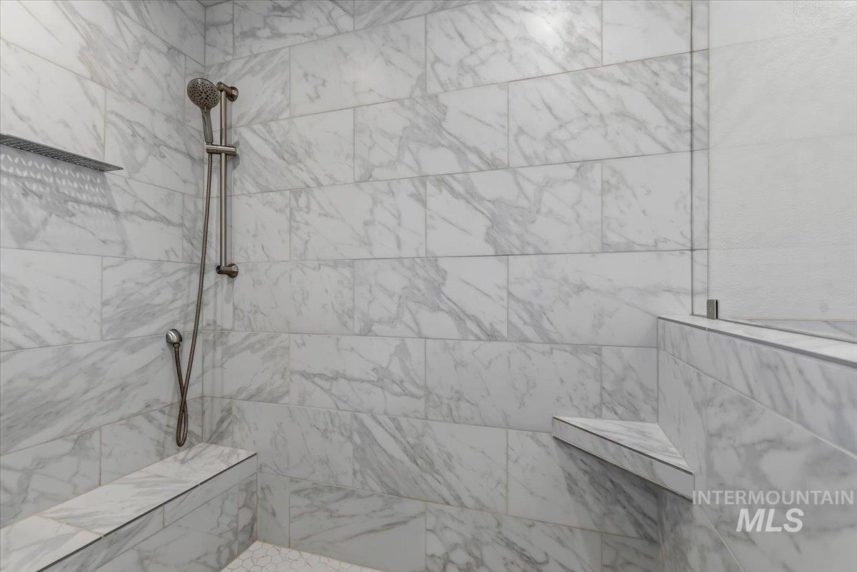12310 West Hidden Point Drive Star, ID 83669 - Photo 16 of 48 Shower featuring large format marble-look tile, rain shower head, handheld shower, built-in bench, and a glass partition Along with custom temperature controls